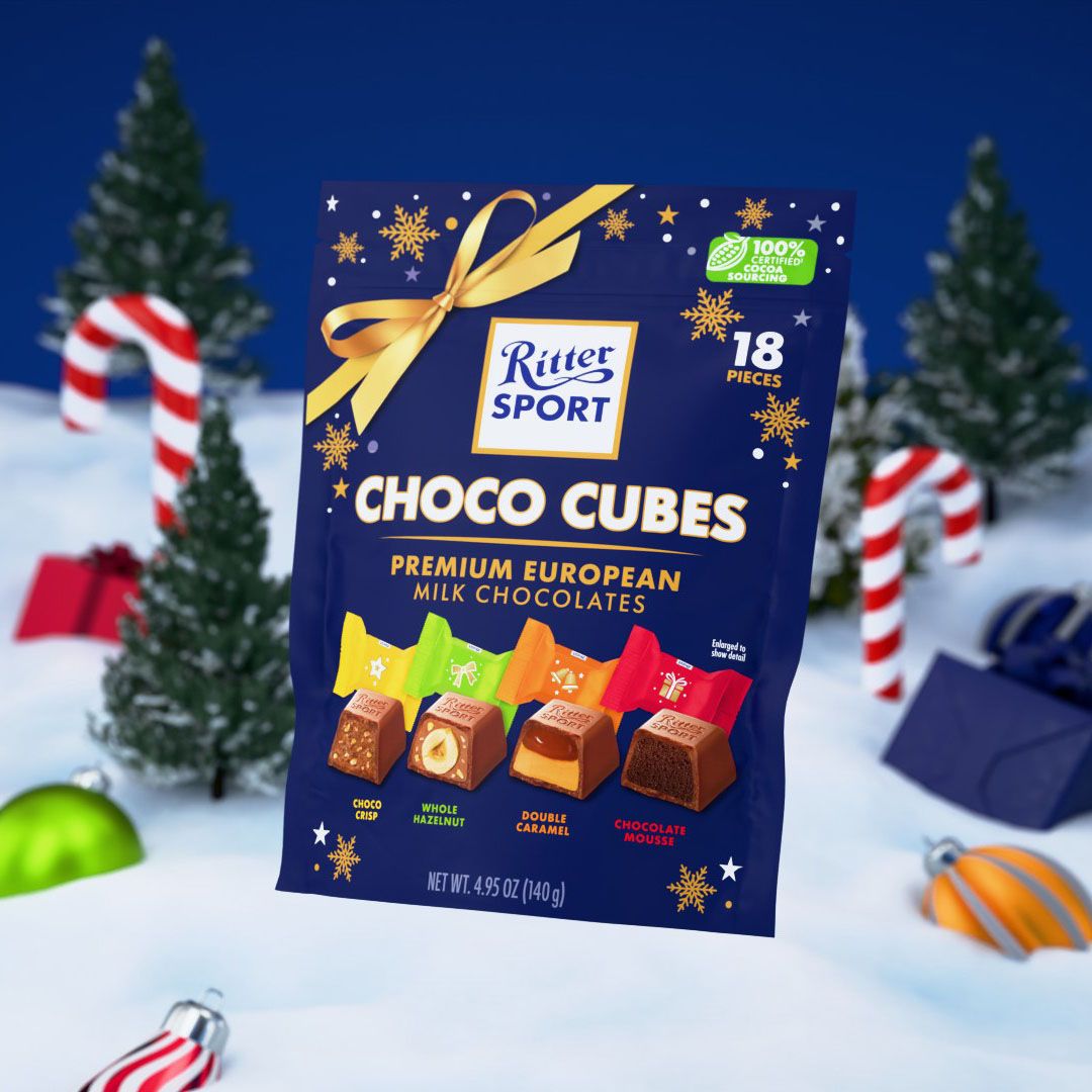 A Ritter Sport Choco Cubes stand-up pouch tied with a gold ribbon, standing in a snowy scene with pine trees, candy canes and baubles, 3D CGI product render