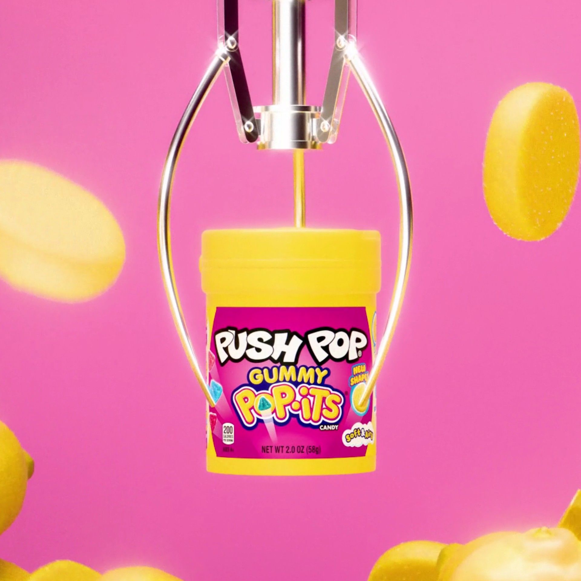 A Push Pop Gummy Pop-Its candy container gripped by a chrome claw against a hot pink background, with yellow gummies flying past, 3D CGI product render