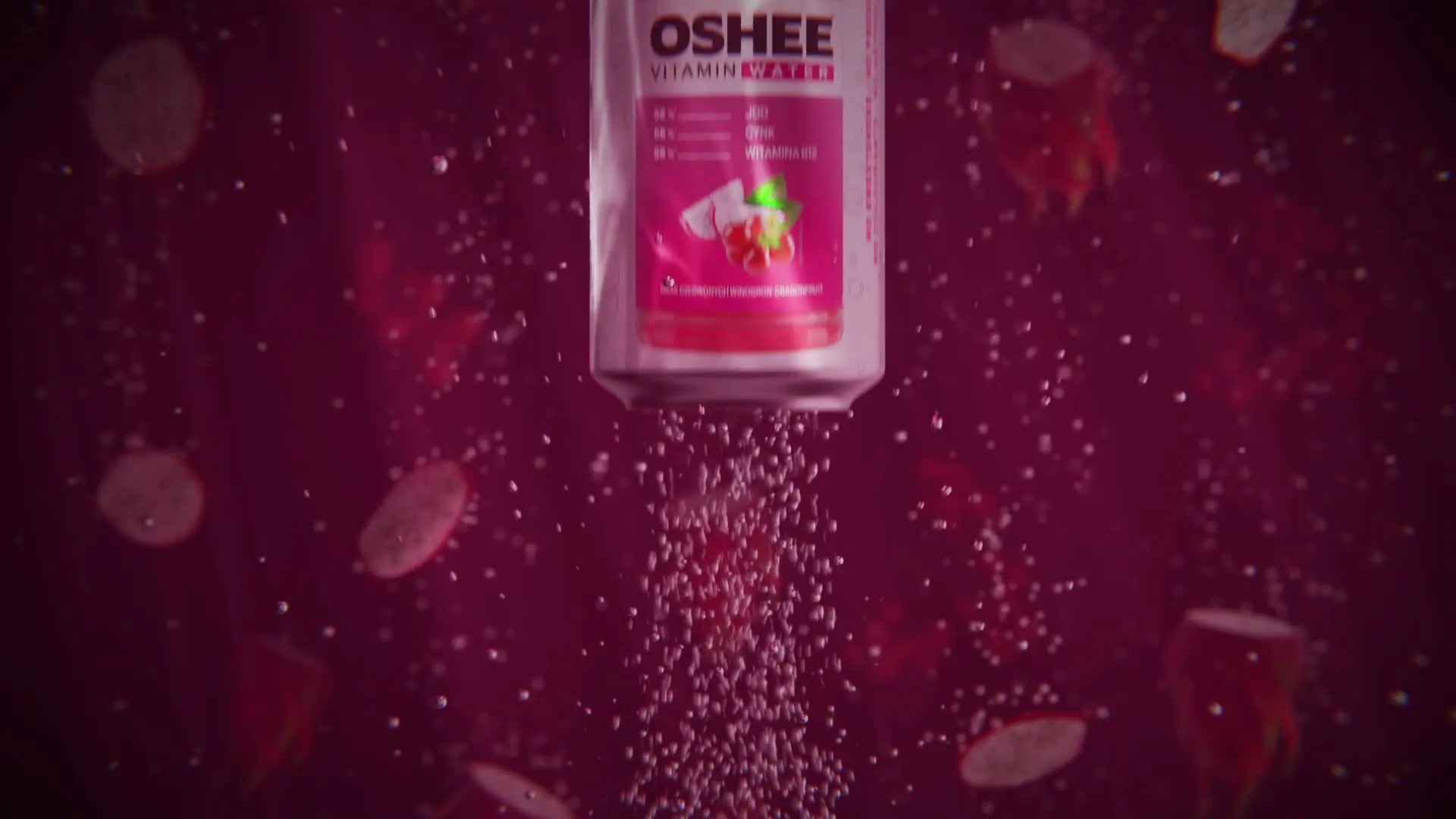 Still from the OSHEE Sparkling Water launch film, a Vitamin Water dragon fruit bottle descending through deep magenta with fruit slices and rising bubbles